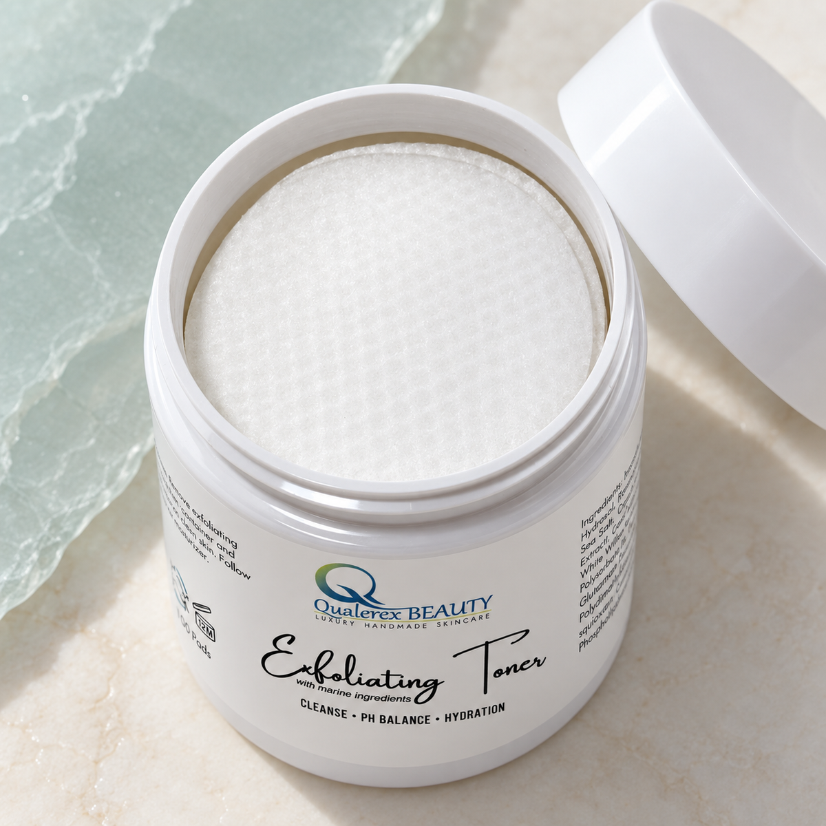 Open jar of Qualerex Beauty Exfoliating Facial Toner Pads showing a soft white pre-soaked pad with the lid beside it.
