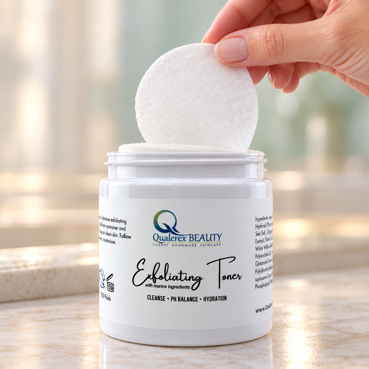 A hand lifts a soft white toner pad from an open jar of Qualerex Beauty Exfoliating Facial Toner Pads.