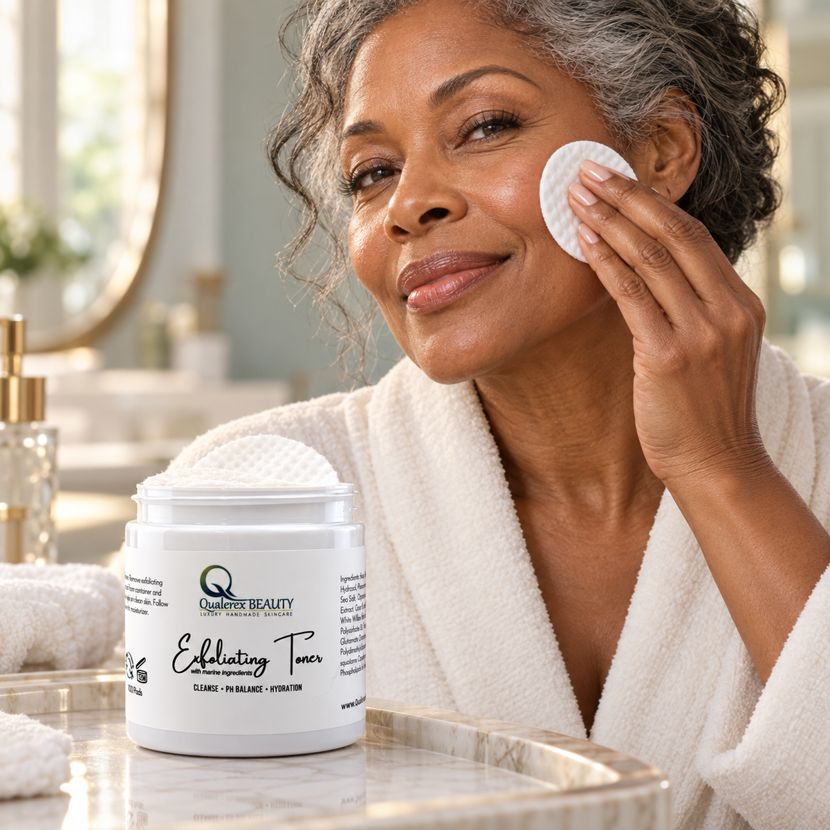 A mature woman gently sweeps a white toner pad across her cheek beside a jar of Qualerex Beauty Exfoliating Facial Toner Pads.