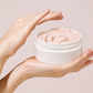 Person holding a jar of pink cream against a light background